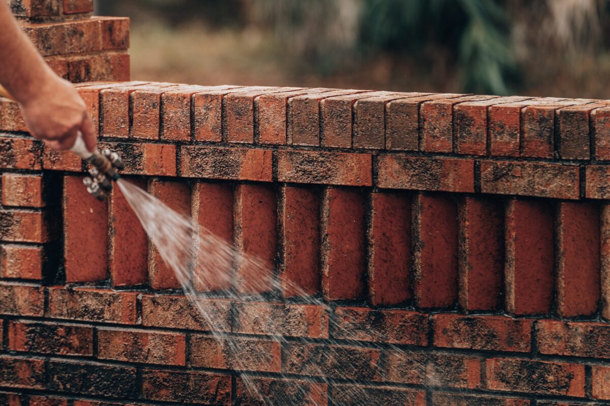 Soft washing a brick wall using low-pressure water to remove dirt and grime, demonstrating the gentle cleaning method.