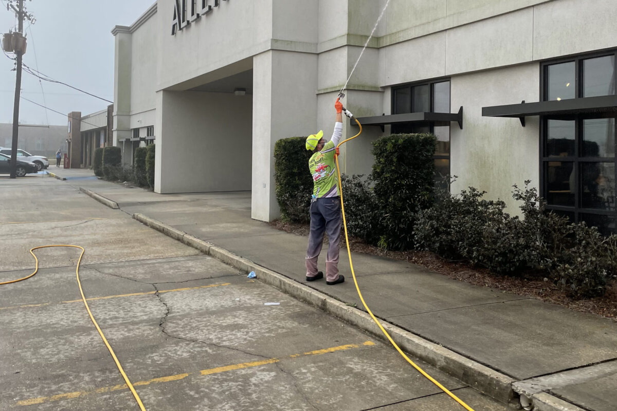 Worker power-washing the exterior of a building with a long hose